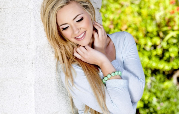 Улыбающаяся блондинка прислонилась к белой стене