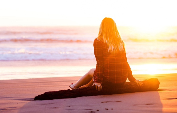 Девушка на сидит на пляже во время заката