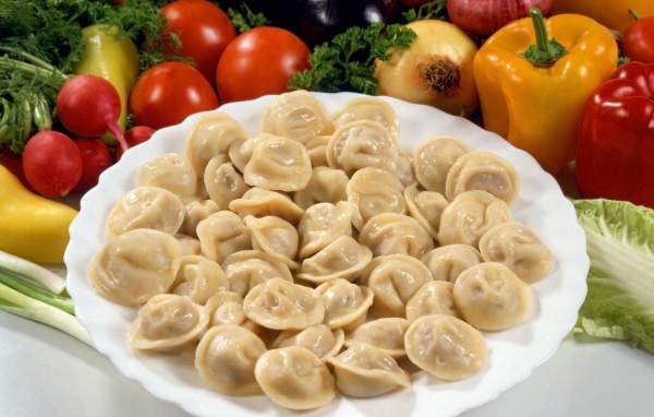 Пельмени на тарелке среди овощей