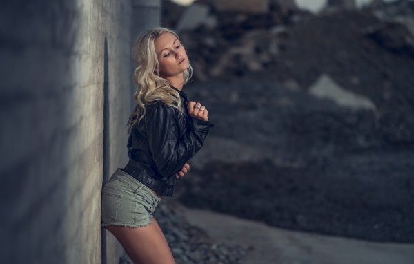 Блондинка в джинсовых шортах стоит у стены