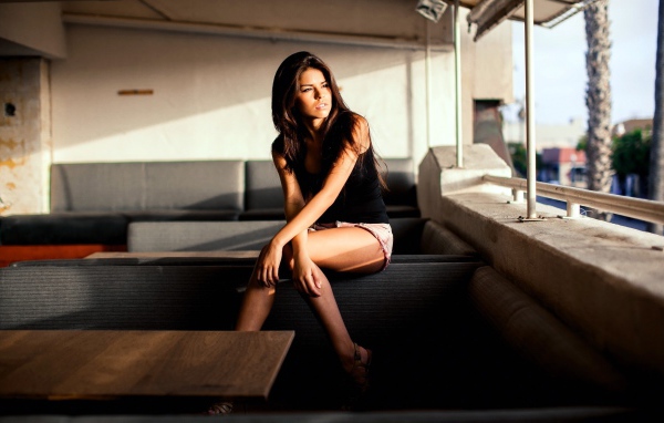 Брюнетка сидит на спинке дивана и смотрит в окно