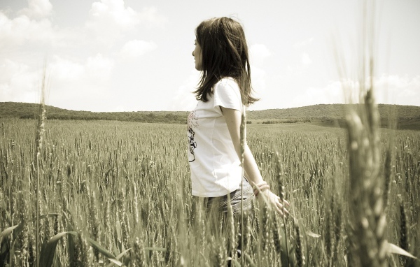 Девушка в белой футболке гуляет по пшеничному полю