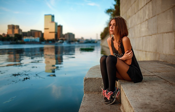 Girl in sneakers sitting on the embankment