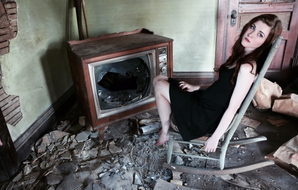 Девушка сидит у разбитого старого телевизора