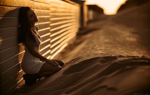 Girl sitting on the sand near the fence