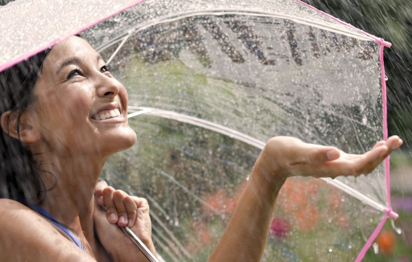 Девушка под прозрачным зонтом ловит дождь рукой