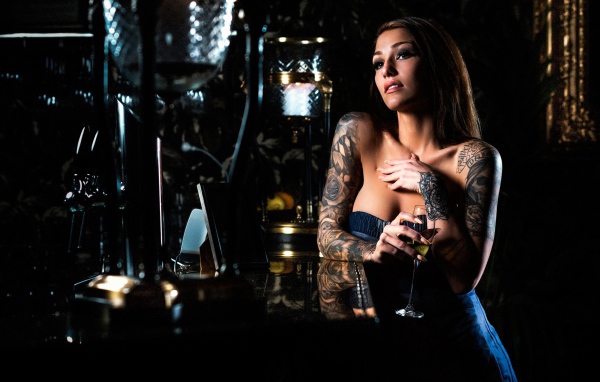 Татуированная девушка пьет вино в баре