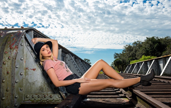 Блондинка в шляпе позирует на железной дороге