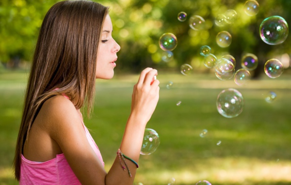 Девушка в розовой футболке запускает мыльные пузыри