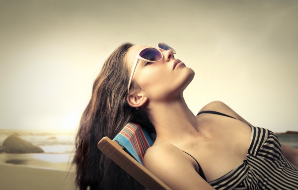 Девушка в очках загорает в шезлонге