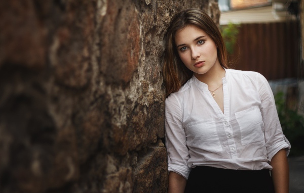 Девушка в белой рубашке стоит у стены