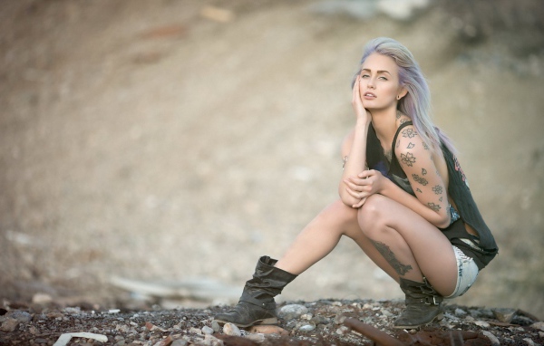 Девушка с татуировками в форме цветов сидит на корточках