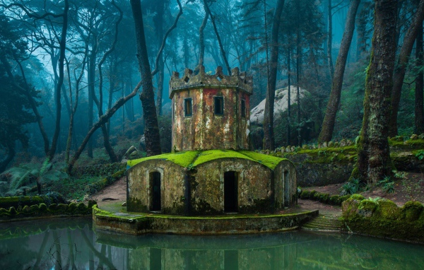 Покрытая мхом каменная беседка у воды