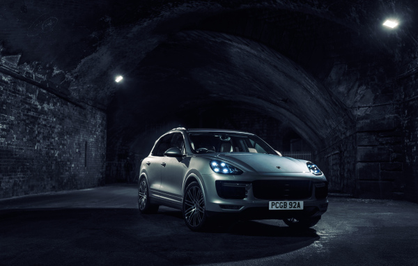 Серебристый автомобиль Porsche Cayenne в тоннеле с включенными фарами