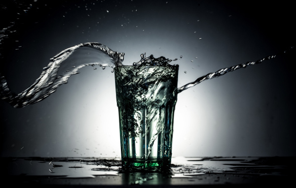 Брызги воды из стакана с водой на сером фоне