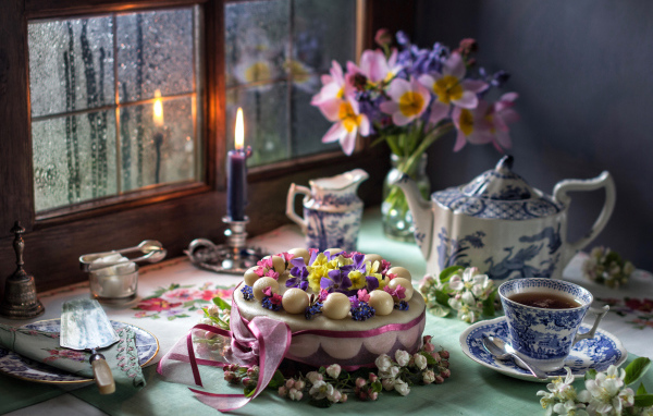 Красивый торт на столе с сервизом и горящей свечой у окна