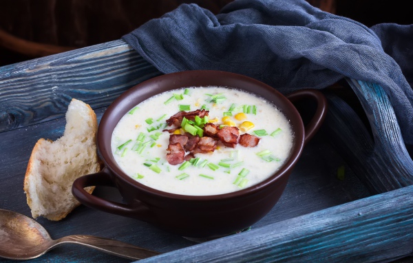 Сырный суп с зеленью и беконом на столе с куском хлеба