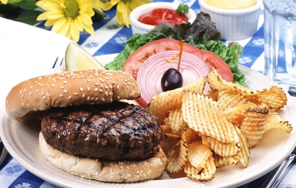 Гамбургер с котлетой и картофельные чипсы на тарелке с овощами