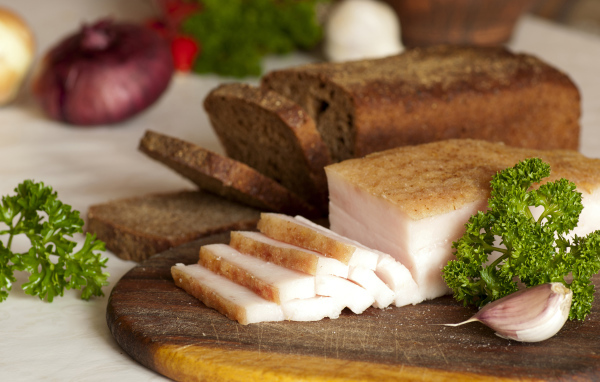 Нарезанное кусочками сало и черный хлеб на разделочной доске