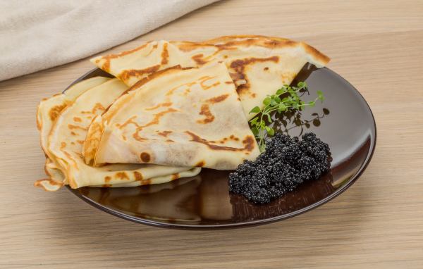 Тонкие блины на тарелке с черной икрой