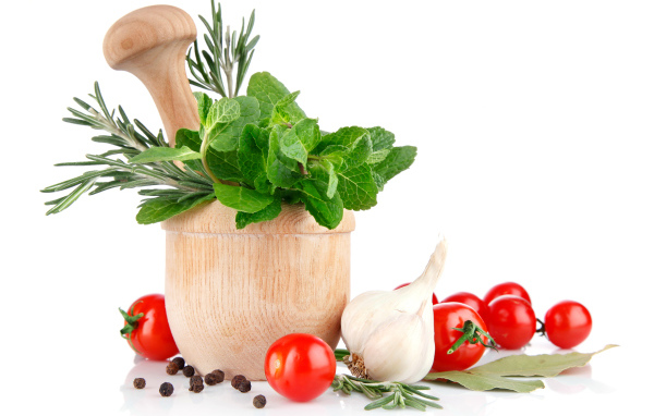 Деревянная ступа и пестик со специями и зеленью на столе с чесноком и помидорами