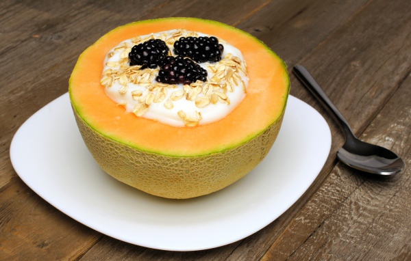 Йогурт с ежевикой и овсянкой в тарелке из свежей дыни на завтрак