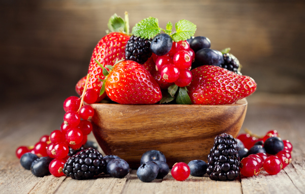 Свежие ягоды смородины, черники и клубники в деревянной тарелке на столе