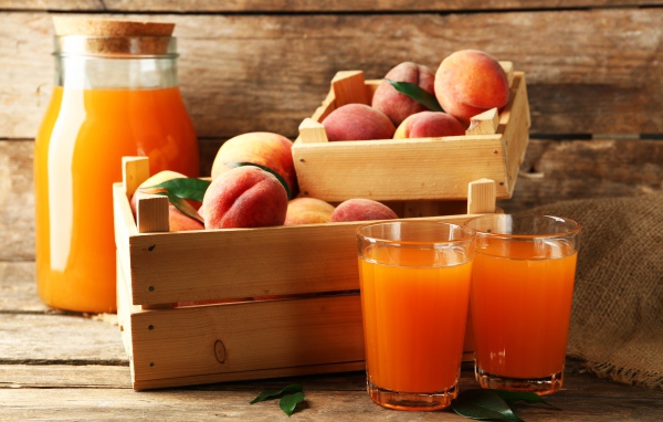 Свежие персики в деревянном ящике со свежим соком на столе