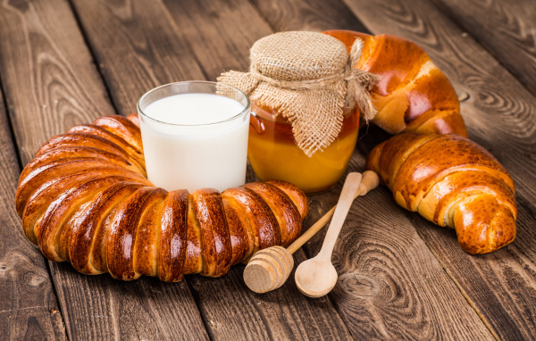 Свежая выпечка на столе со стаканом молока и медом