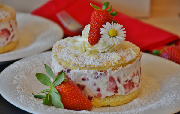Торт со сливочным кремом и свежими ягодами клубники на белой тарелке