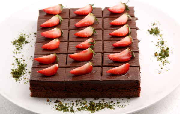 Шоколадное пирожное со свежей клубникой на белой тарелке