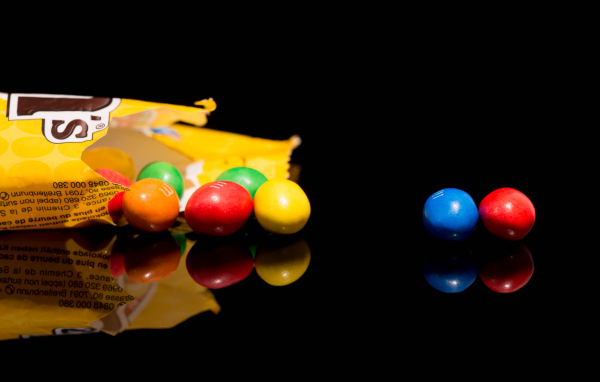 Разноцветные конфеты  M&m's отражаются в черной поверхности стола 