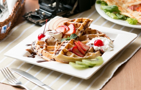 Сладкие вафли с ягодами клубники, вишни и кусочками киви на тарелке