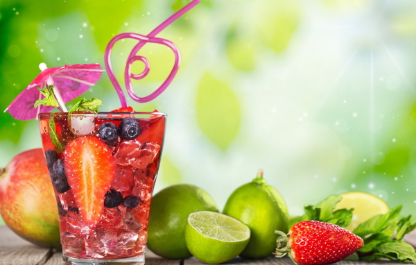 Коктейль с клубникой и ягодами черники в стакане со льдом на столе с лаймами и клубникой