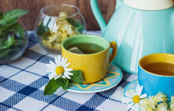 Чай с цветами ромашки в желтой чашке на столе