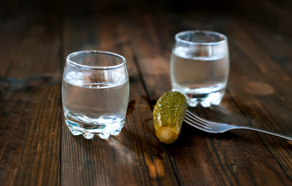 Две рюмки водки и соленый огурец на столе