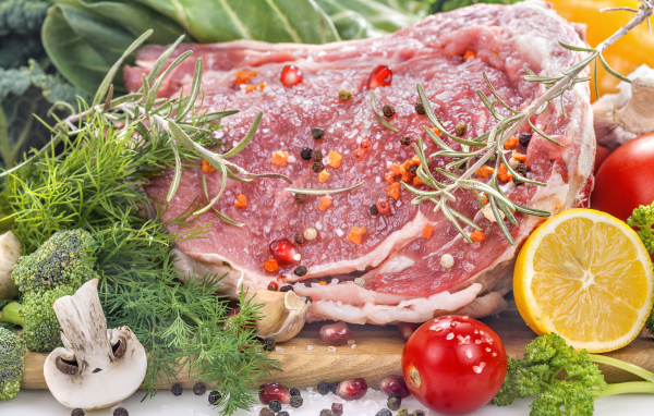 Кусок свежего мяса со специями и зеленью на разделочной доске