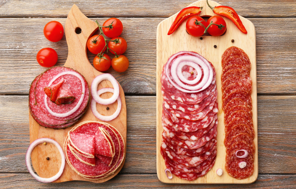 Аппетитная колбасная нарезка на разделочной доске с кольцами лука