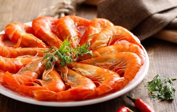 Аппетитные вареные креветки на тарелке с зеленью петрушки