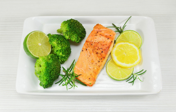 Красная рыба на белой тарелке с лимонами и брокколи