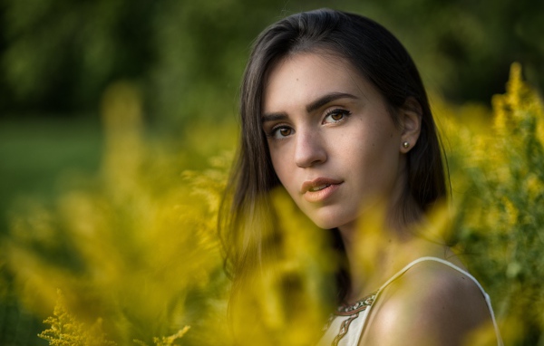 Красивая девушка с нежным взглядом сидит у желтых цветов