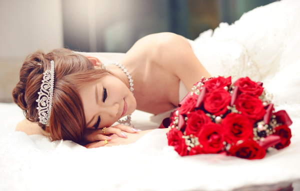 Красивая девушка азиатка в свадебном платье с букетом красных роз