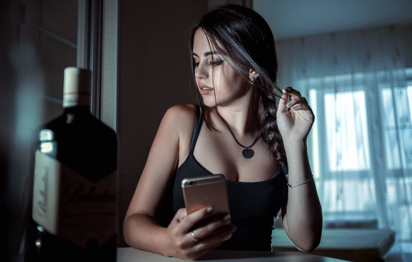 Красивая брюнетка с телефоном в руках и бутылкой