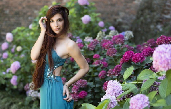 Красивая девушка модель в зеленом платье рядом с цветами гортензии