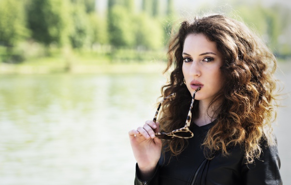 Красивая девушка с волнистыми волосами с очками в руках 