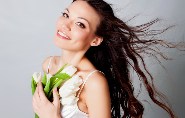 Красивая улыбающаяся брюнетка с букетом тюльпанов на сером фоне