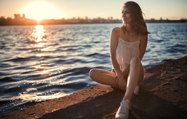 Красивая улыбающаяся девушка сидит в лучах солнца у реки