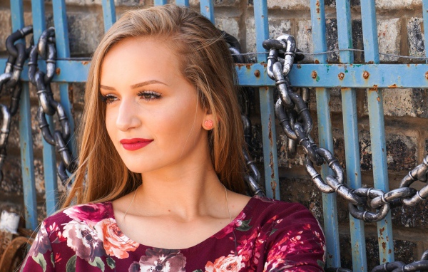 Красивая молодая девушка сидит у забора с железными цепями