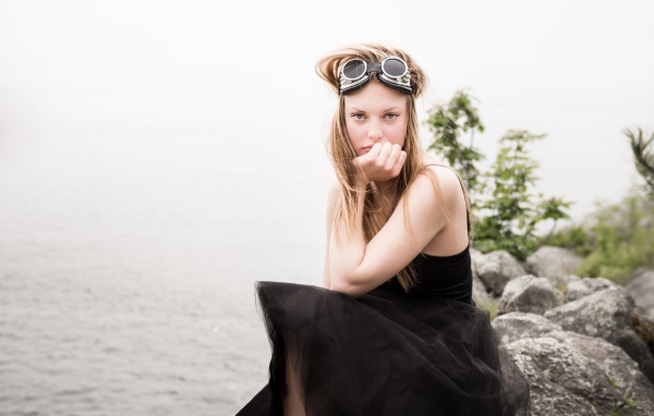 Девушка блондинка с очками на голове сидит на камне