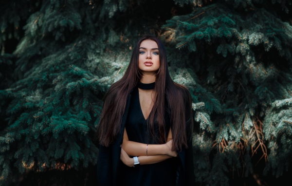 Голубоглазая девушка брюнетка у большой зеленой ели 
